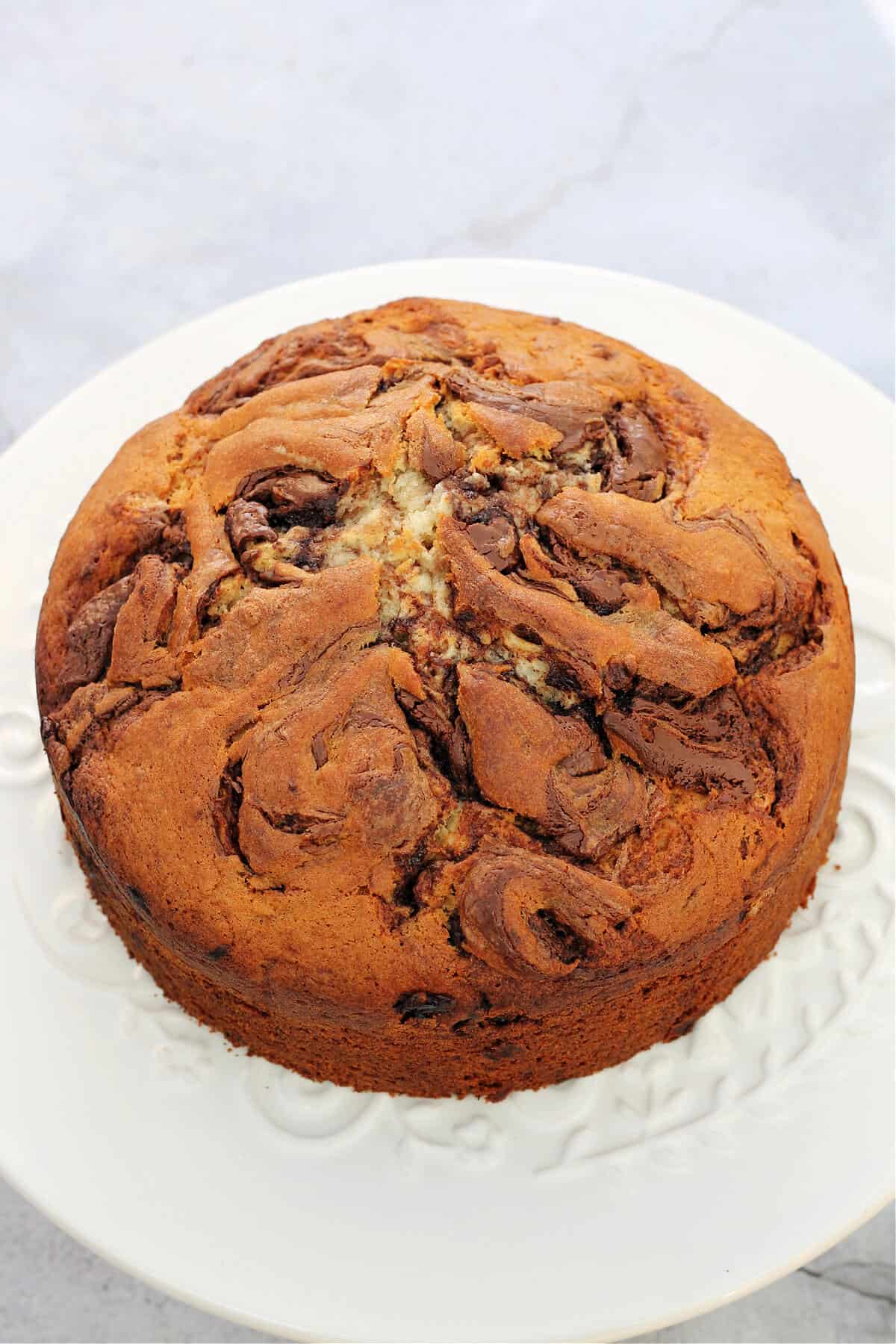 Banana cake with swirls of Nutella on top, on white cake stand.