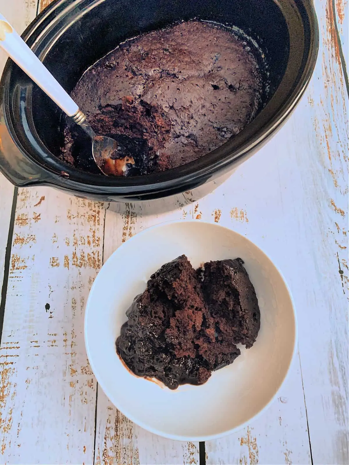 A slow cooker with chocolate lava cake and a spoon, and a bowl of the dessert in front of it.