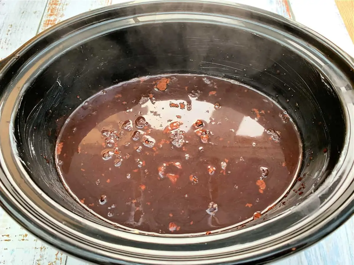 View of slow cooker pot after pouring the sauce ingredients over the cake mixture.