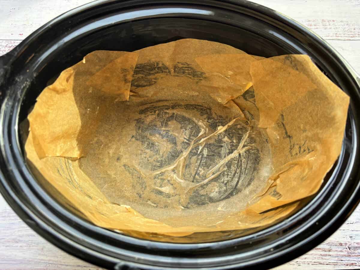 Slow cooker pot lined with baking paper.