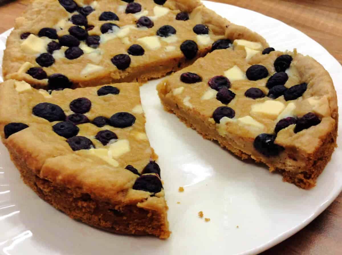 Giant cookie cut into pieces on a white plate.