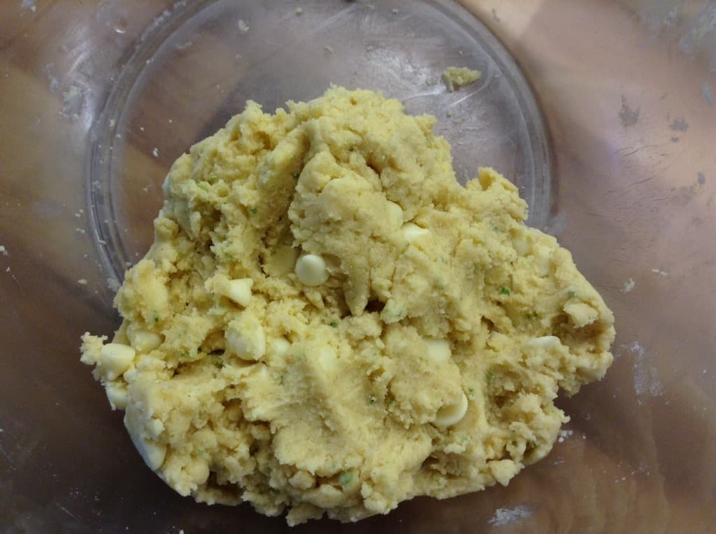 Shortbread dough with white chocolate chips mixed in, in clear bowl.