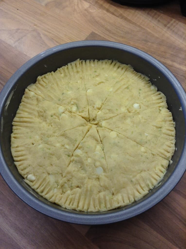 Shortbread dough with white chocolate chips mixed in, in clear bowl.