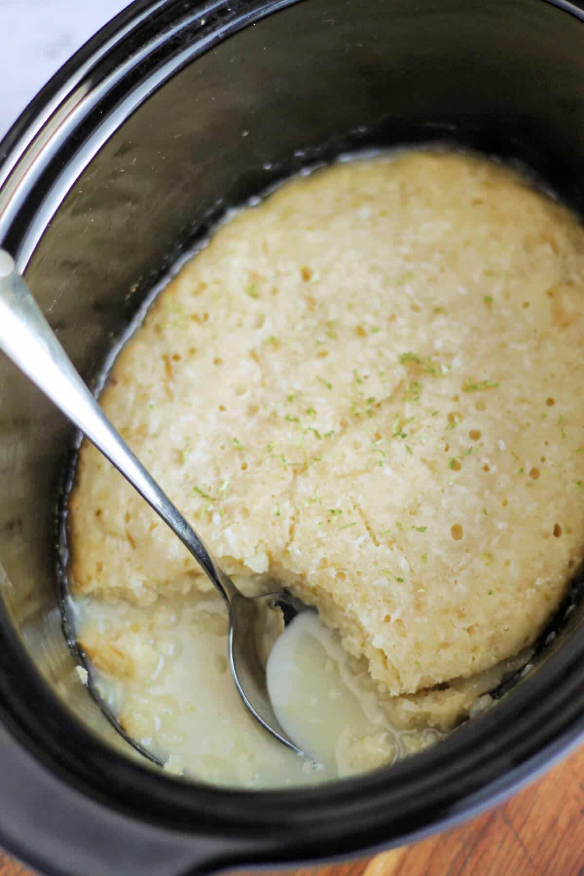Lime pudding with lime sauce in slow cooker pot, with a serving spoon.