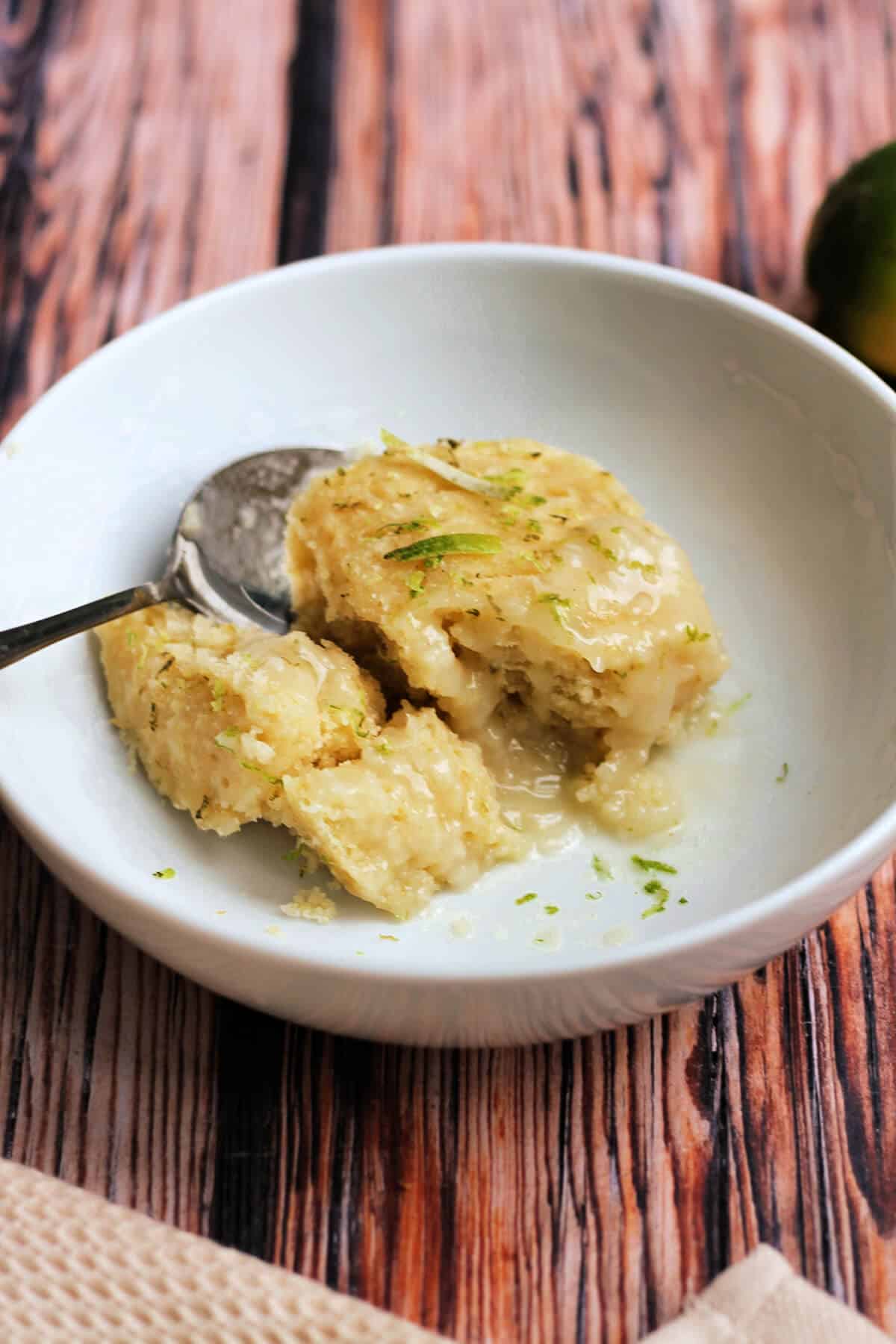 Bowl of coconut and lime self-saucing pudding, with spoon.