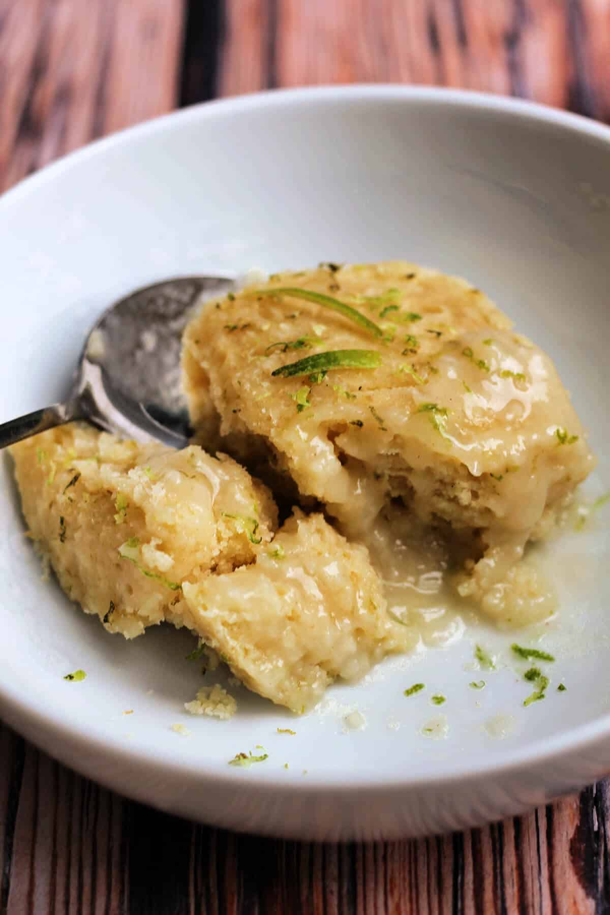 Close up of soft lime coconut sponge with lime sauce in a white bowl.