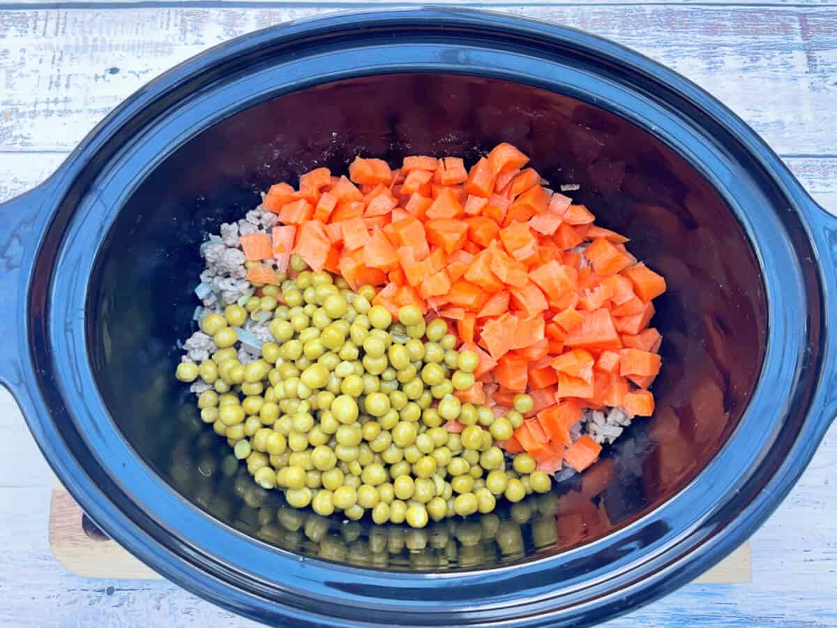 Slow cooker pot with peas and diced carrot.