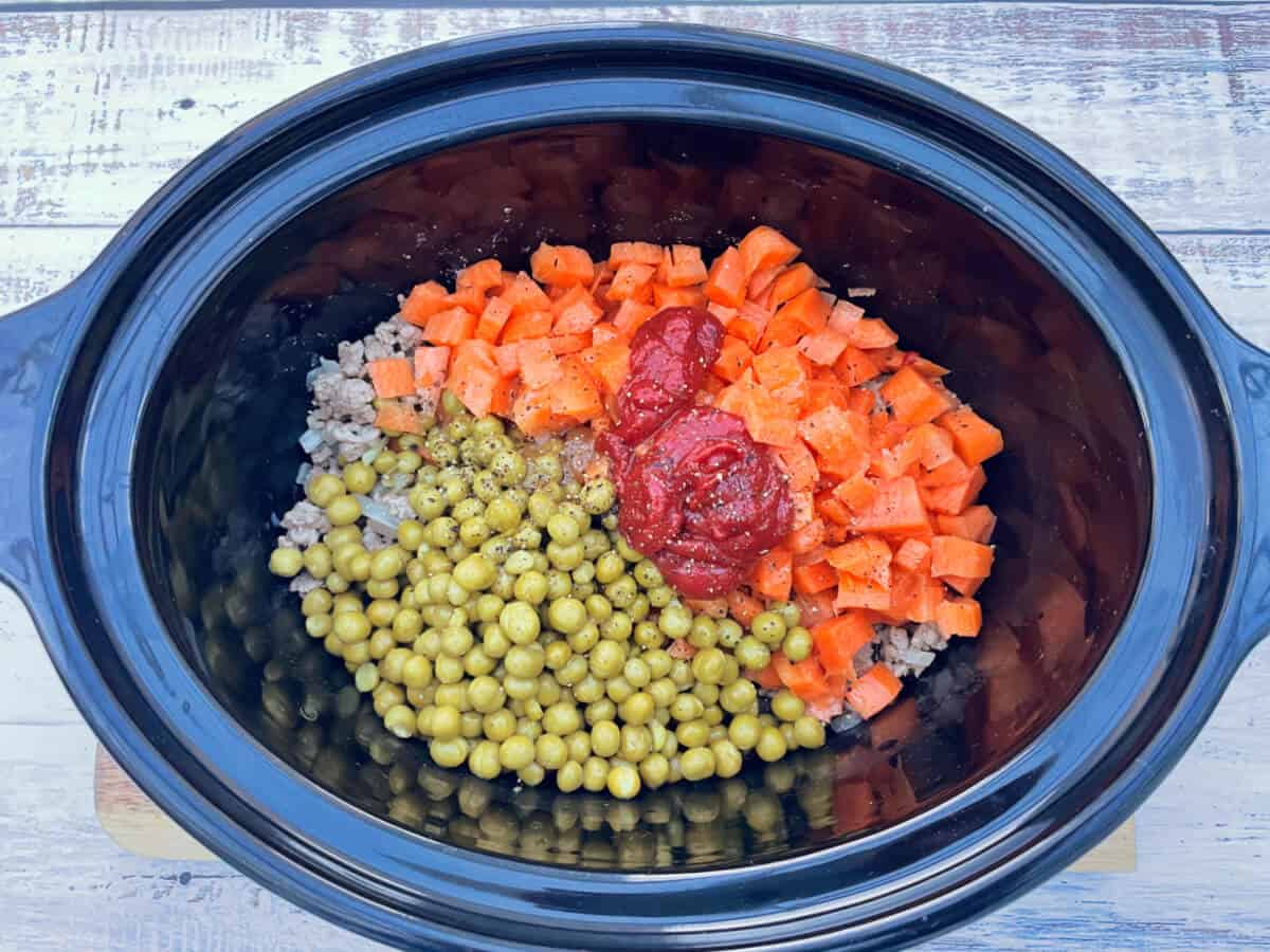 Ingredients in slow cooker pot, with tomato puree and seasoning on top.