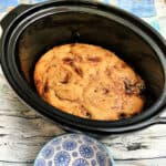 Jam sponge pudding in slow cooker pot, with blue patterned bowl to the side.