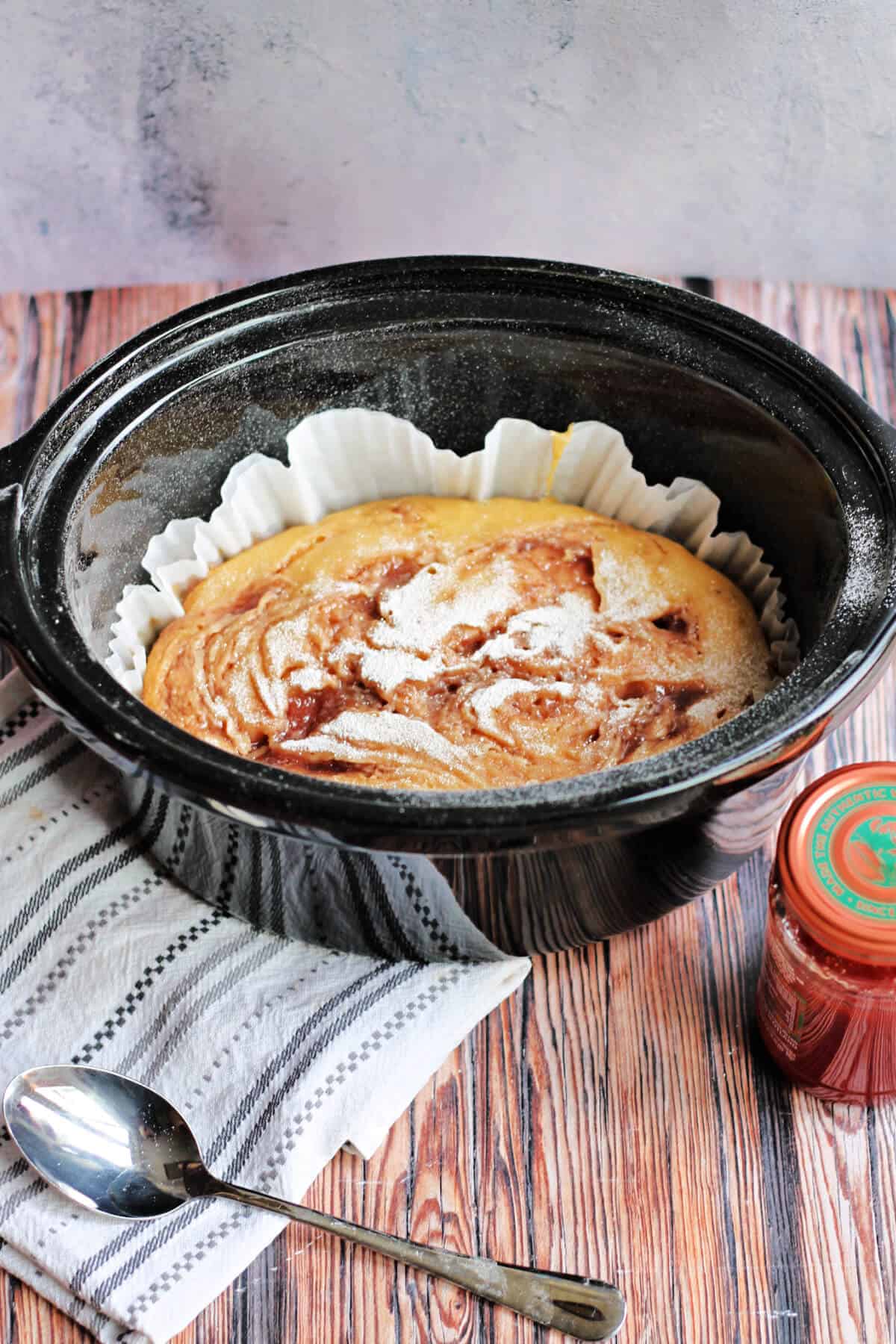 Jam swirl cake in slow cooker pot, spoon and jam to the side.