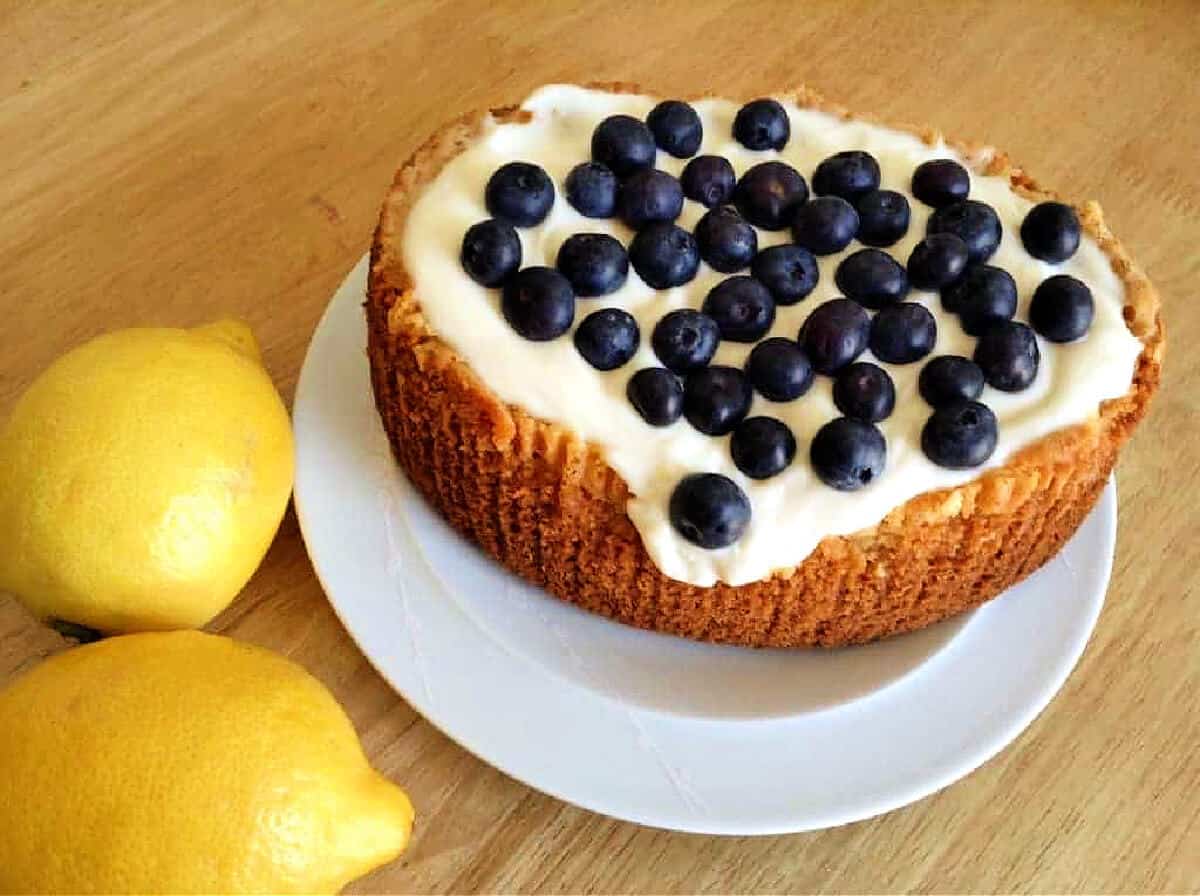 A cake on a white plate with cream icing and topped with blueberries.