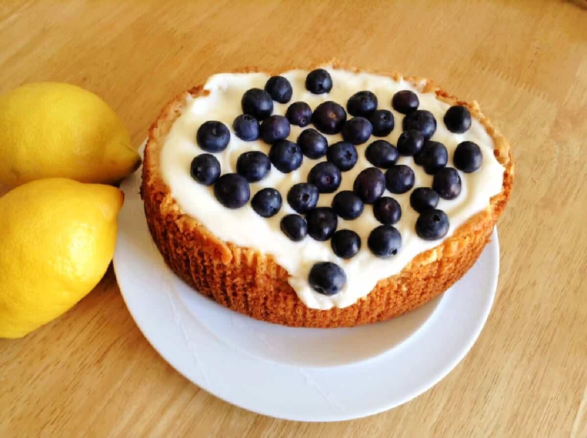 A cake on a white plate with cream icing and topped with blueberries.