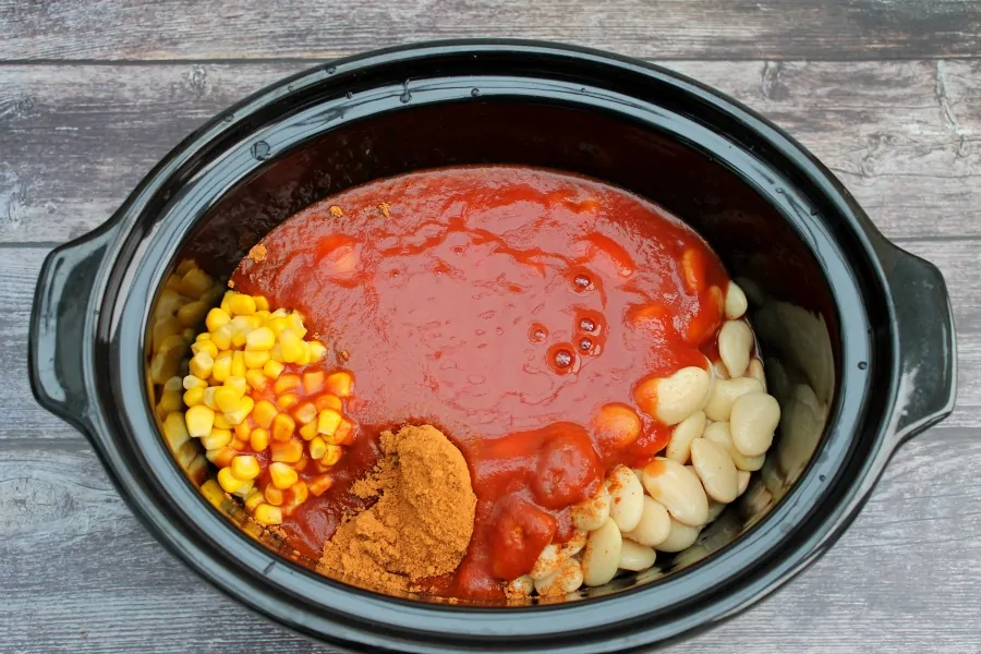 Overhead view of crockpot with chicken and tomato sauce plus beans and spices