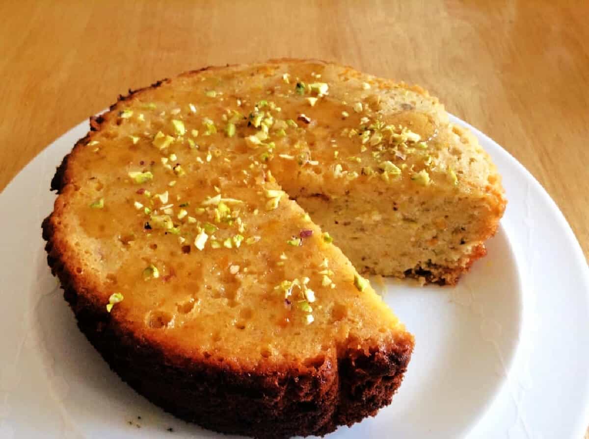 Orange and honey cake topped with chopped pistachios, on a white plate.
