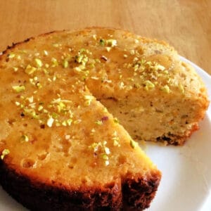 Orange and honey cake topped with chopped pistachios, on a white plate.