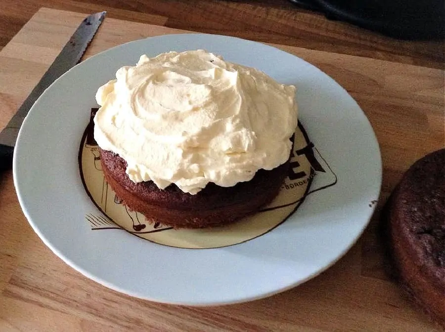 One half of a cake on a plate with whipped cream spread as a filling.