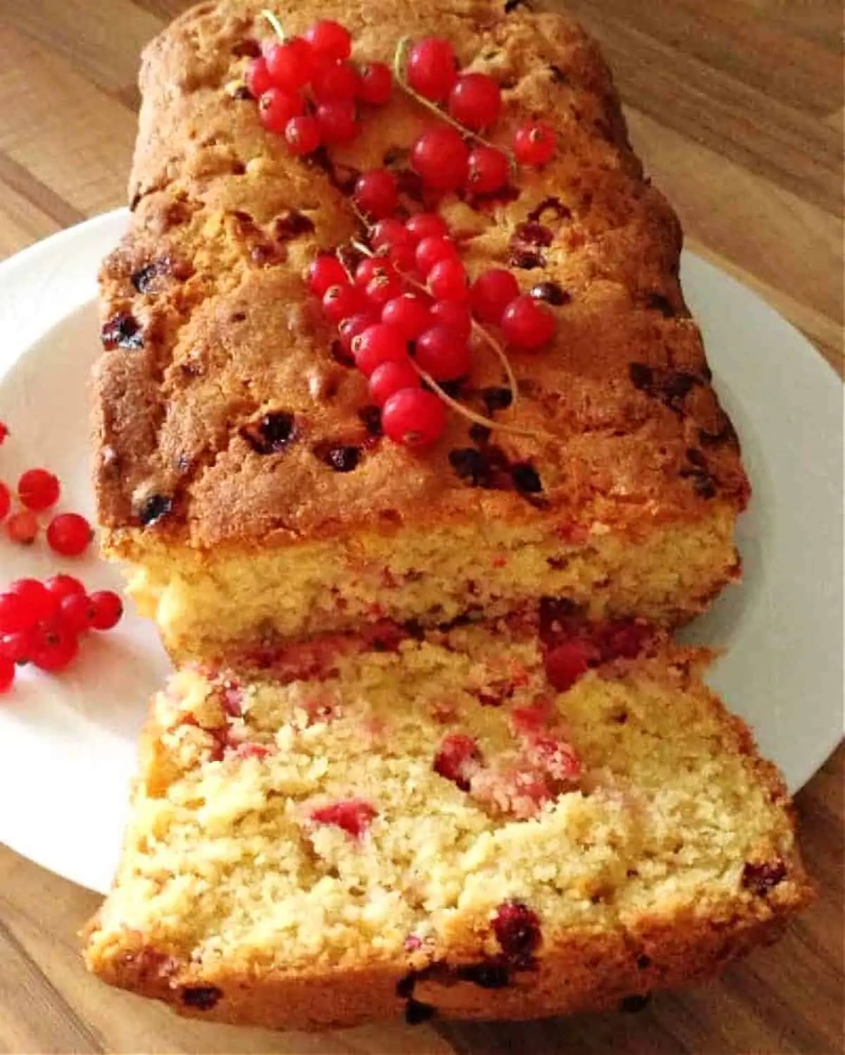 A loaf cake filled with redcurrant cut open on a white plate.