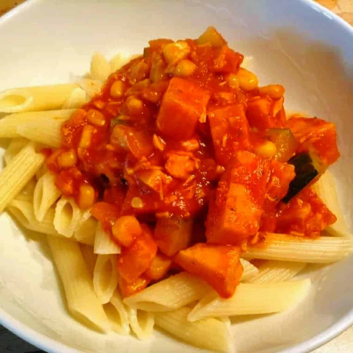 Bowl of penne pasta topped with chicken and veg stew.