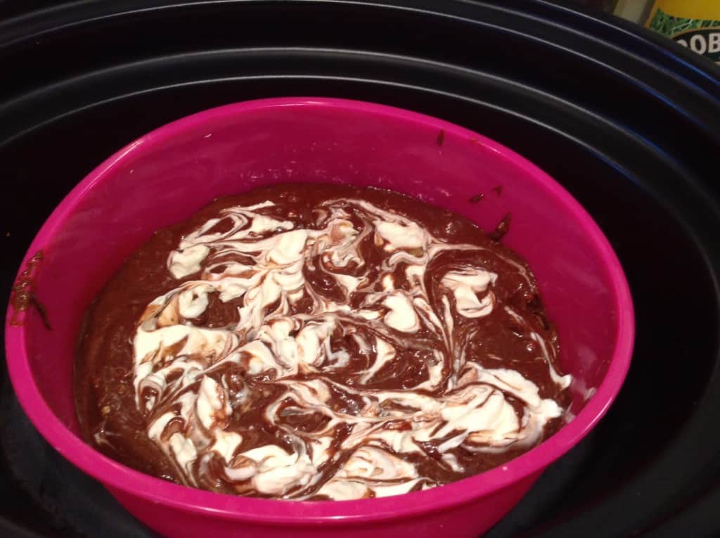 Brownie batter marbled with cream cheese in silicone pan in slow cooker pot.