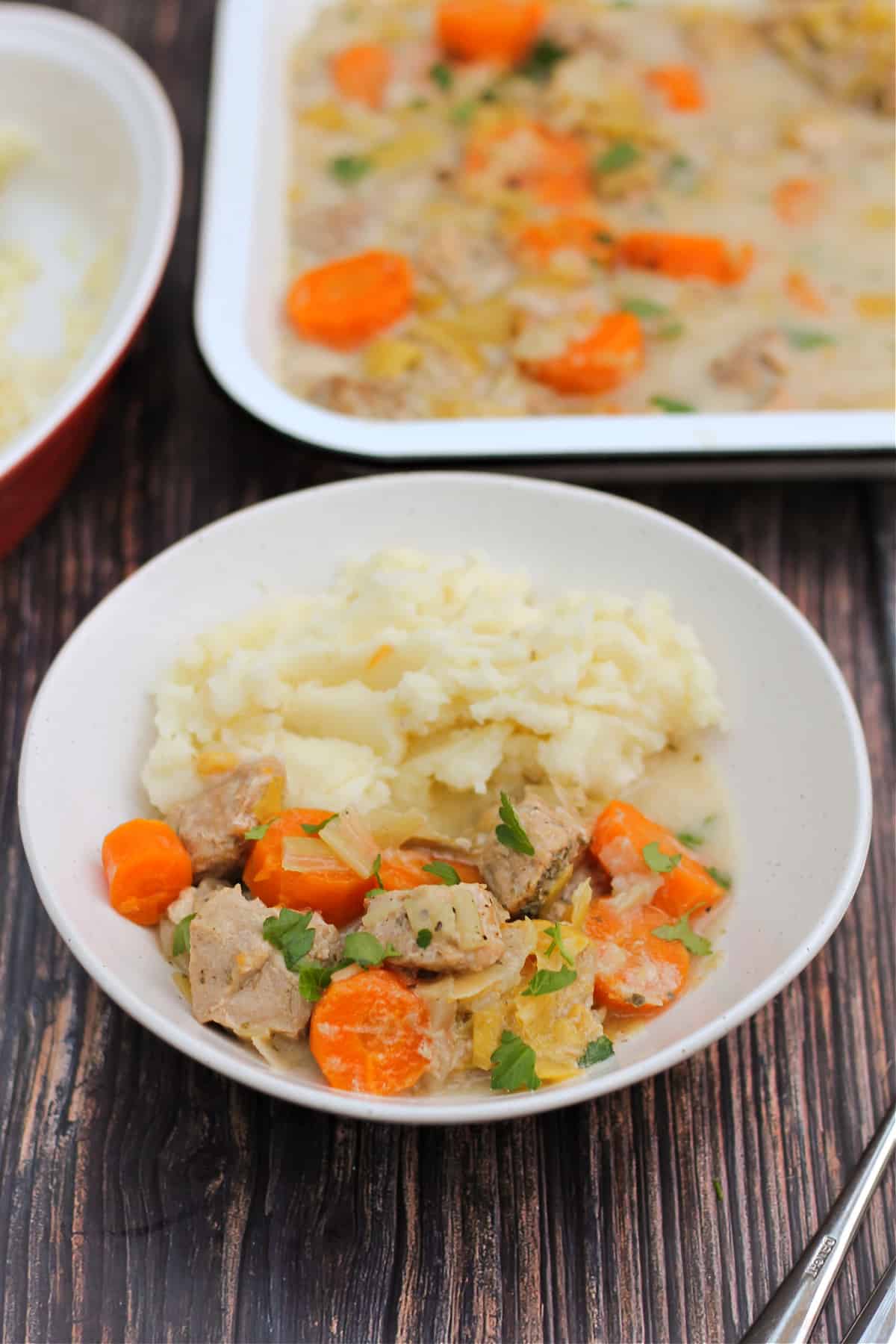White bowl of pork casserole with carrots and mash.