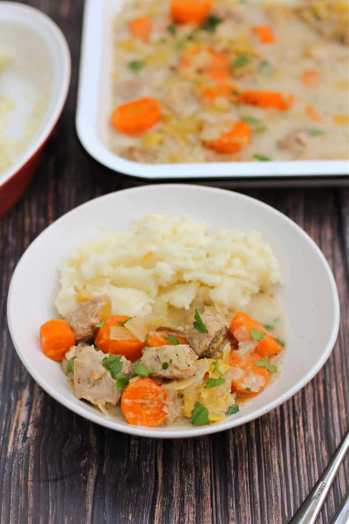 White bowl of pork casserole with carrots and mash.