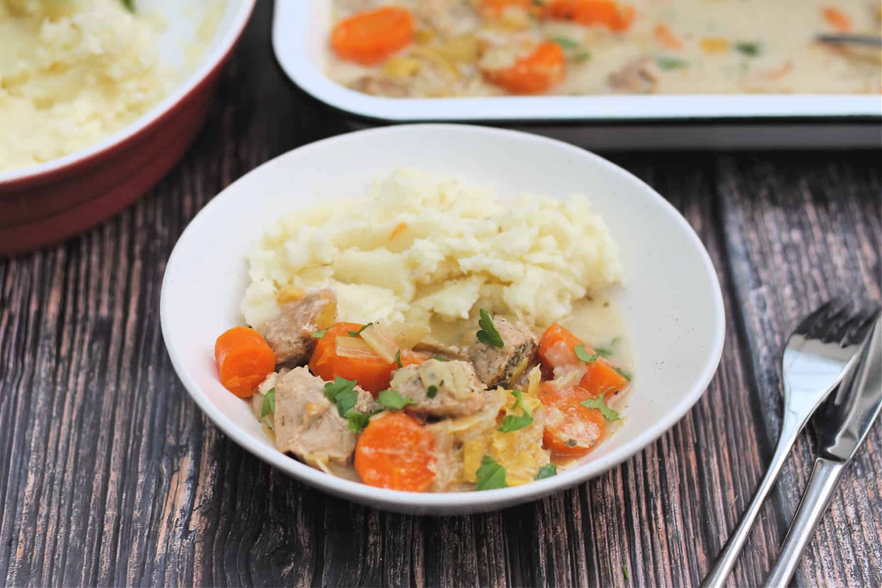 Bowl of pork casserole with cutlery beside.