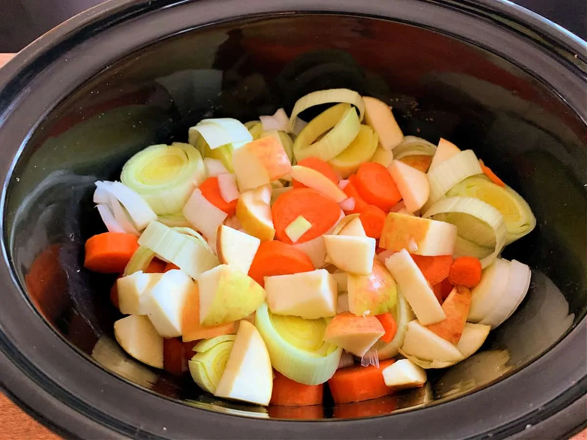 Sliced vegetables in slow cooker pot.