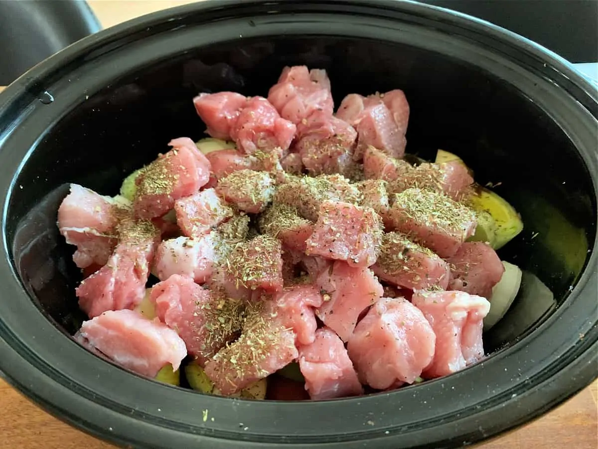 Pork with herbs on top of vegetables in slow cooker pot.