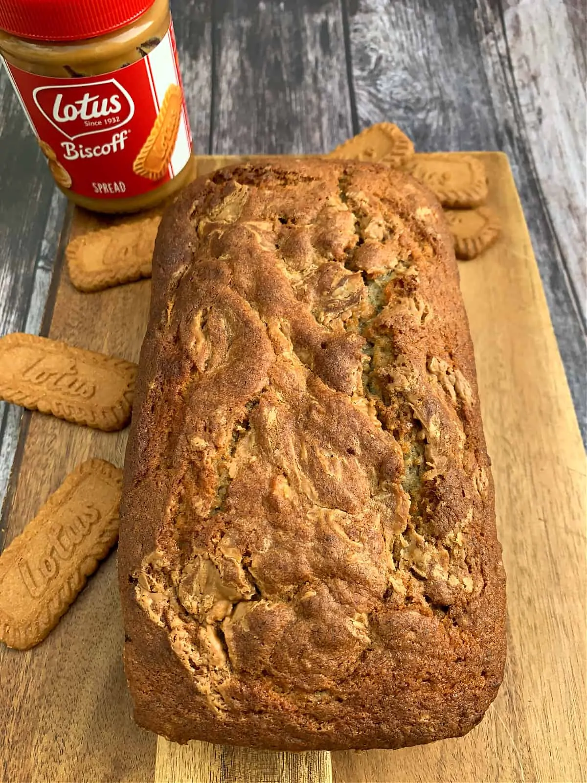 Banana bread on a wooden board with Biscoff biscuits and spread to the side.