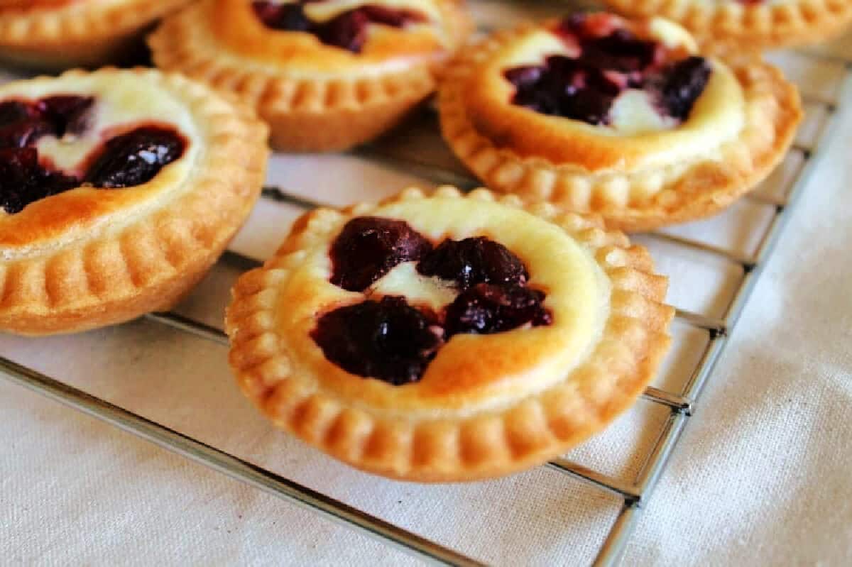 Little pies with cheesecake filling toped with cranberries, on cooling rack.