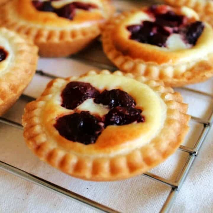 Little pies with cheesecake filling toped with cranberries, on cooling rack.