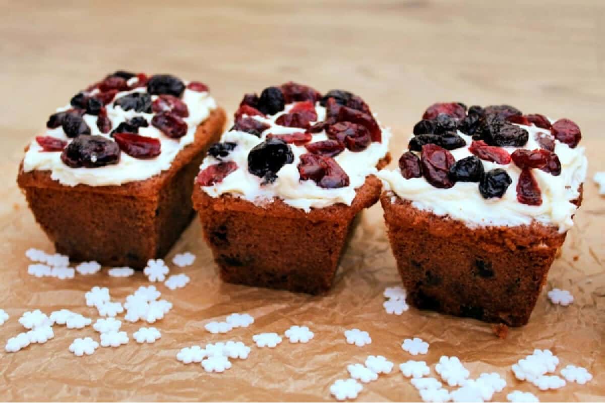 Side view of three small ginger cakes with berries on top of vanilla buttercream.