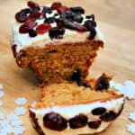 Small ginger loaf cake cut in half showing the soft inside, with white icing and berries on top.