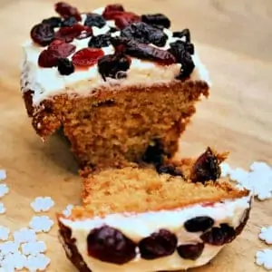 Small ginger loaf cake cut in half showing the soft inside, with white icing and berries on top.