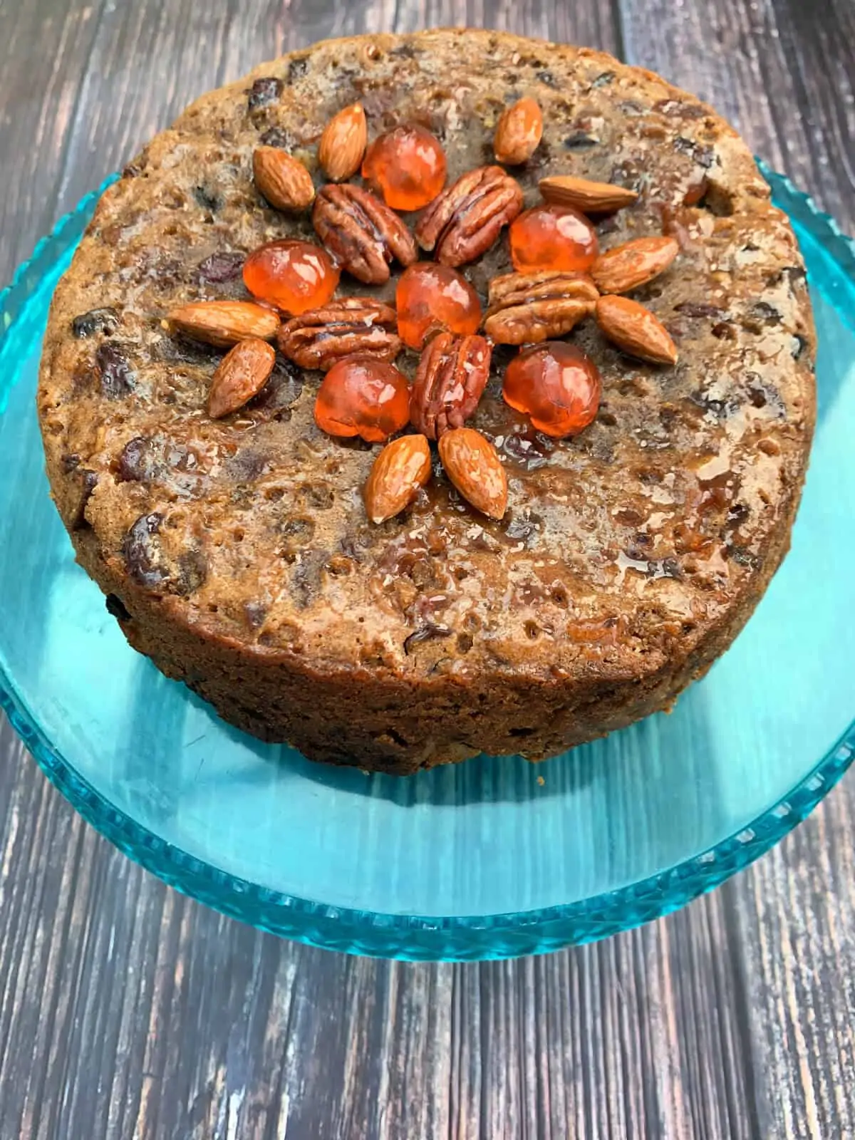 Christmas fruit cake decorated with fruit and nuts on a blue cake stand.