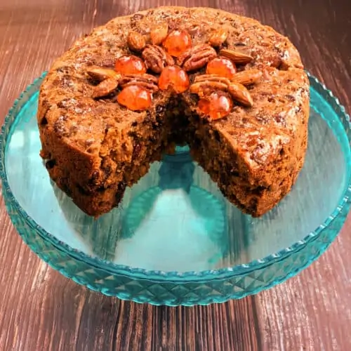 Close up of a Christmas Cake with nuts on top on a blue cake stand, one slice cut out.