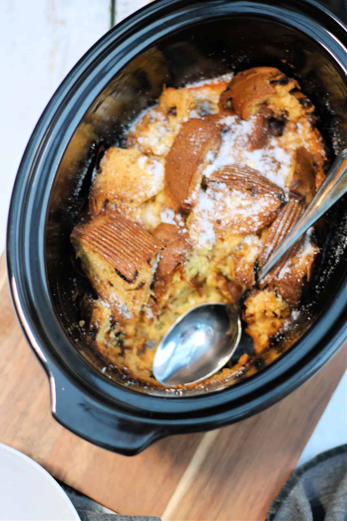 Panettone pudding in slow cooker pot with serving spoon.