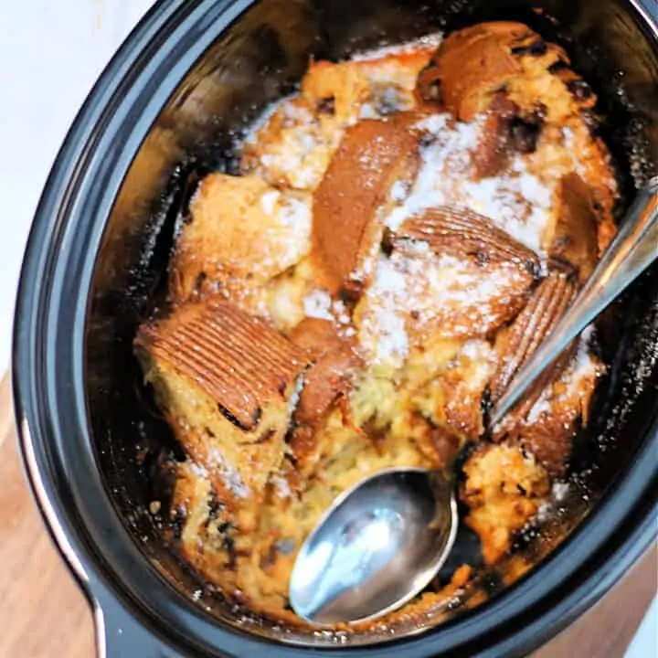 Panettone pudding in slow cooker pot with serving spoon.