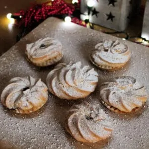 Close up of mince pies dusted with icing sugar on a wooden board.