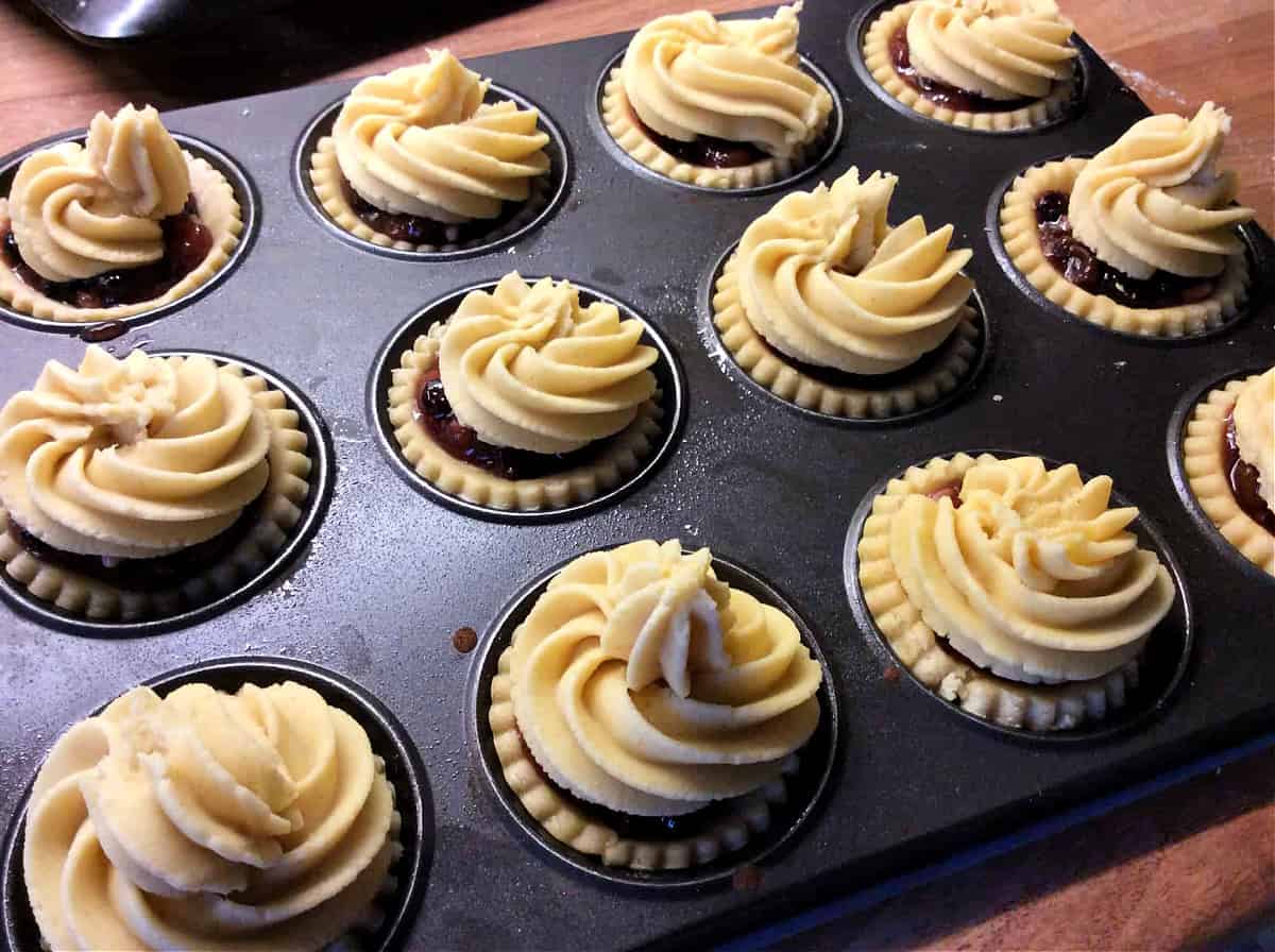 Mince pies with viennese topping swirls, in baking tray before cooking.