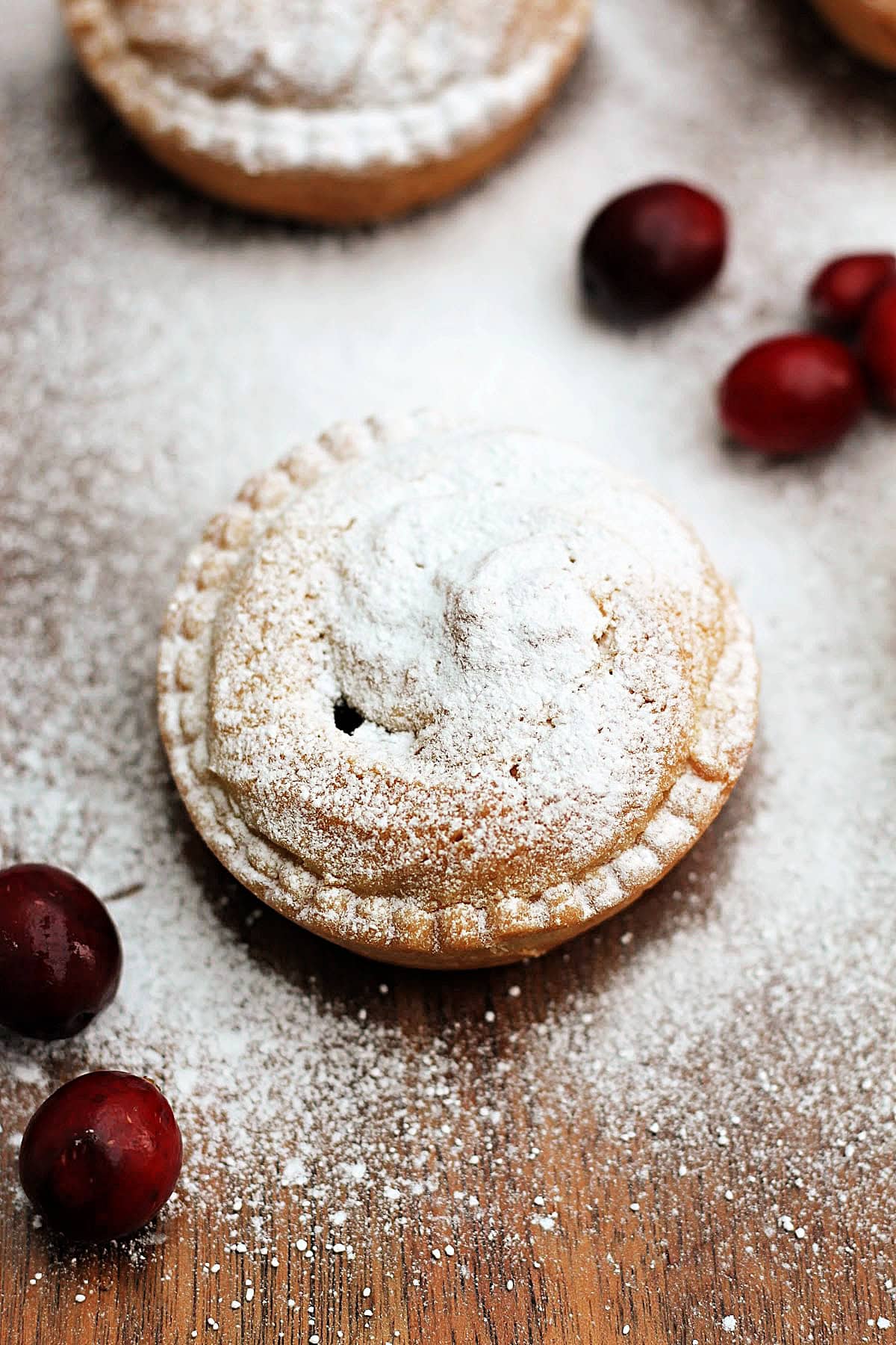 A viennese mince pie topped with icing sugar, with fresh cranberries next to it.
