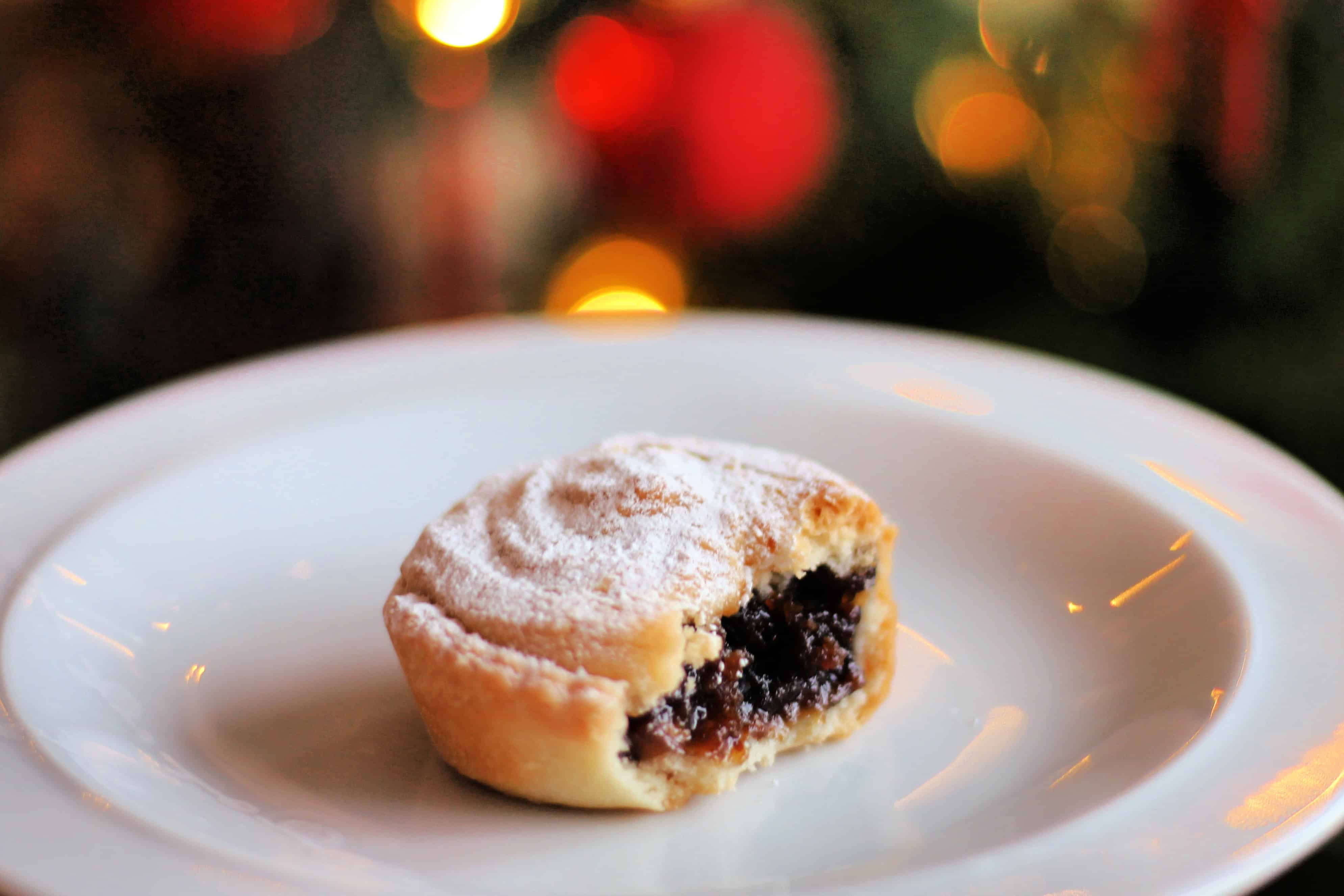 Mince pie bitten open, on a white plate with festive lights in background.
