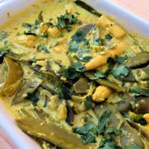 Close up of yellow and green veg curry in a white dish.