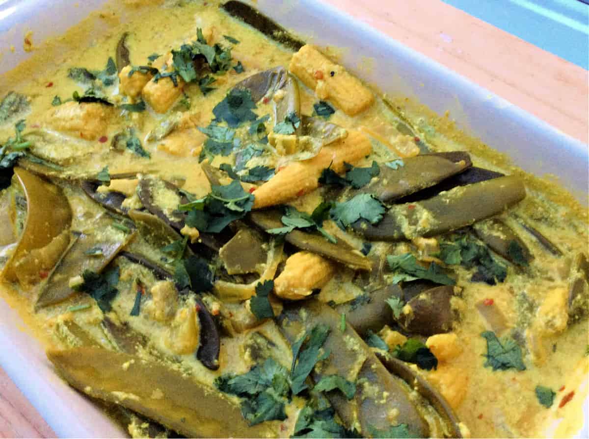 Close up of yellow and green veg curry in a white dish.