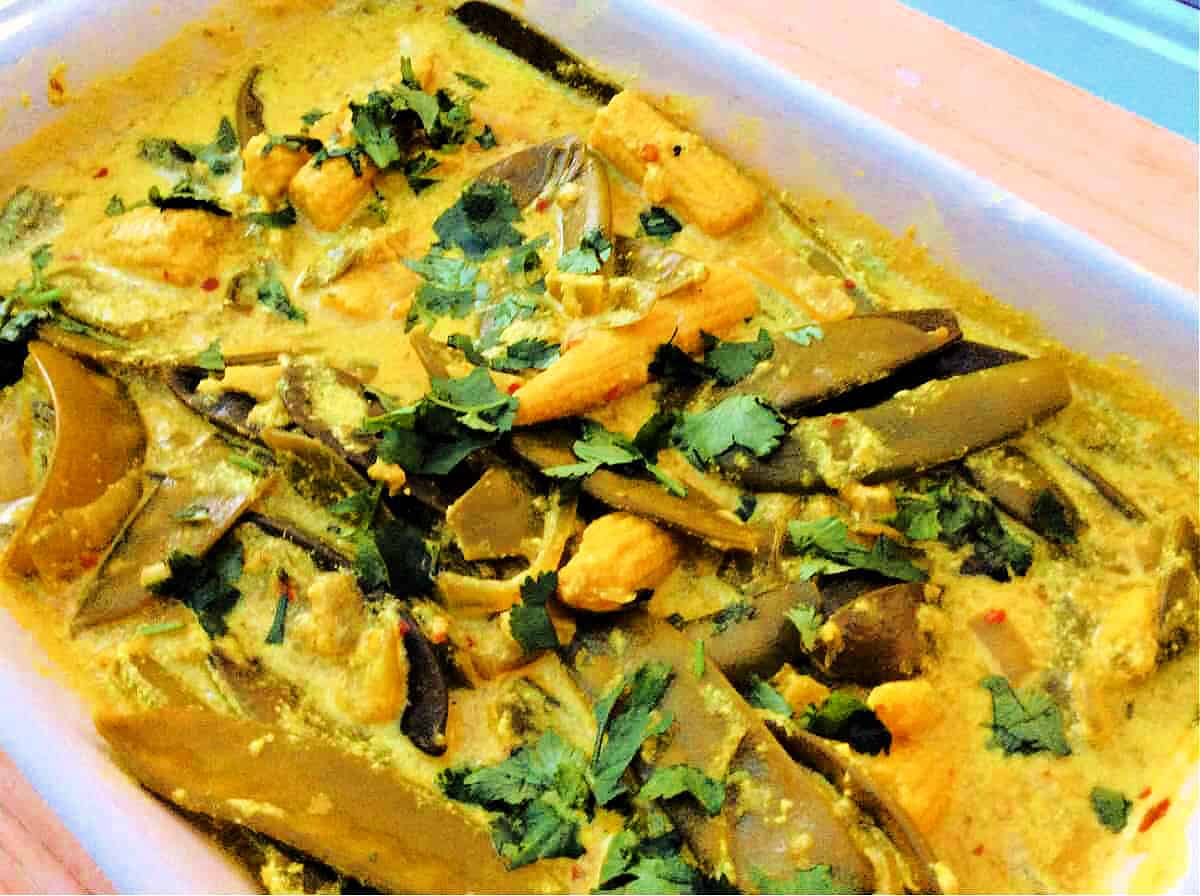 Close up of yellow and green veg curry in a white dish.