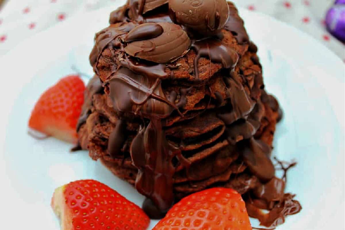 A stack of pancakes with drizzled chocolate and strawberries.