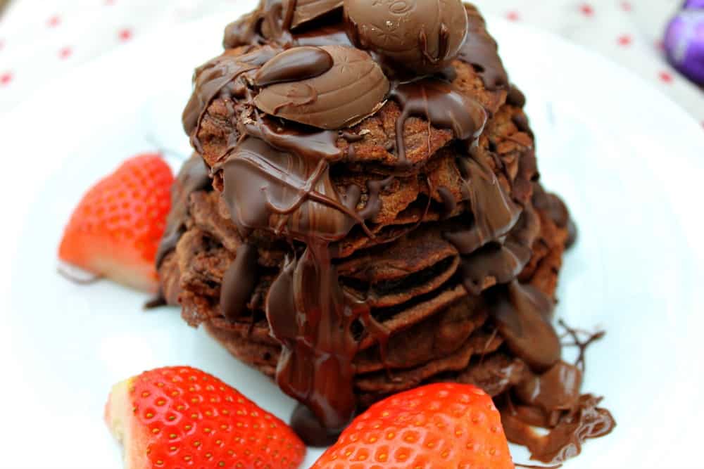 Tower of Nutella pancakes with chocolate drizzled over and strawberries on the side.