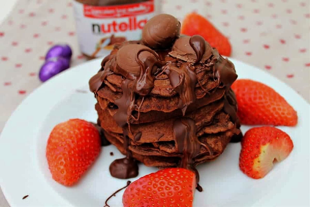 A stack of pancakes with drizzled chocolate and strawberries.