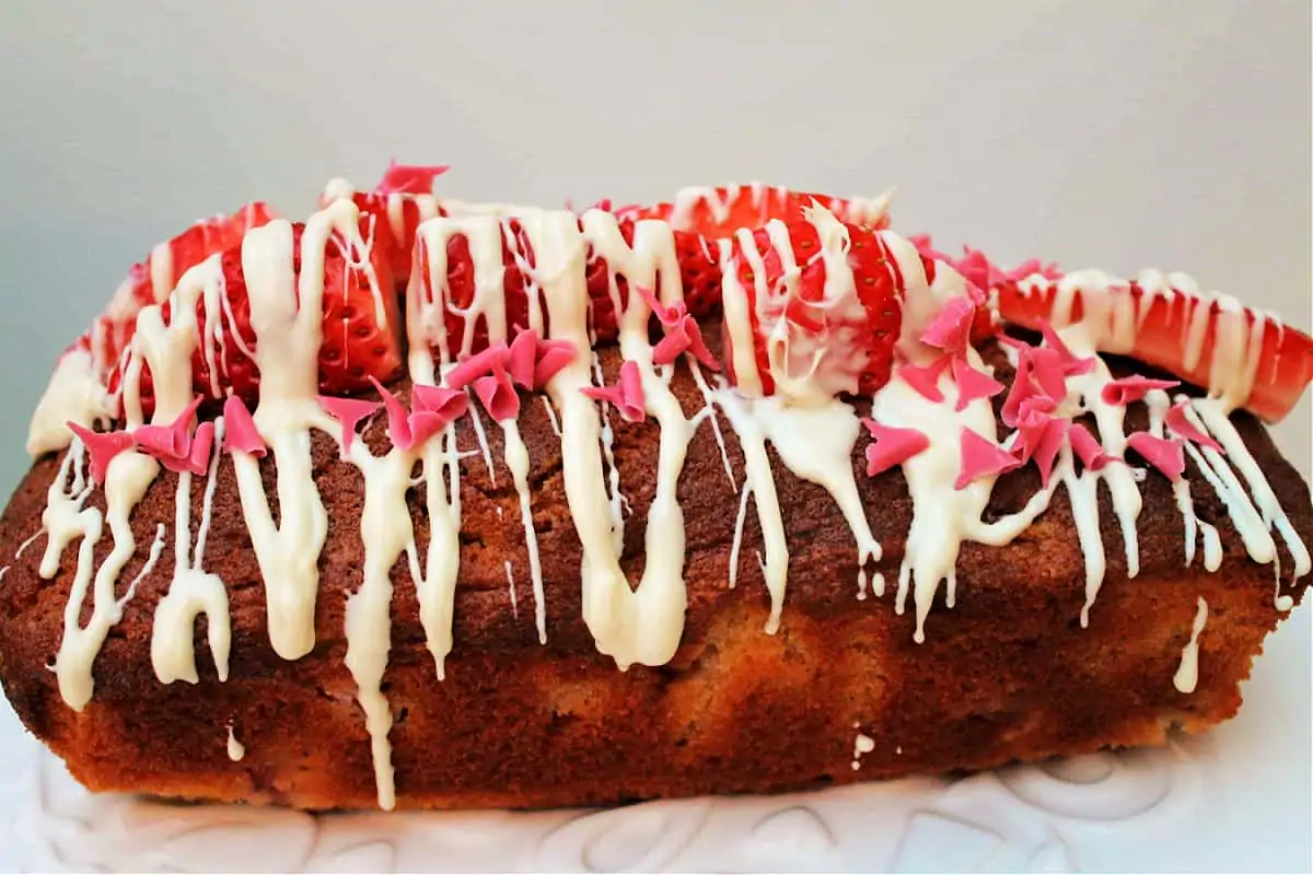 Side view of loaf cake decorated with strawberries and melted white chocolate.