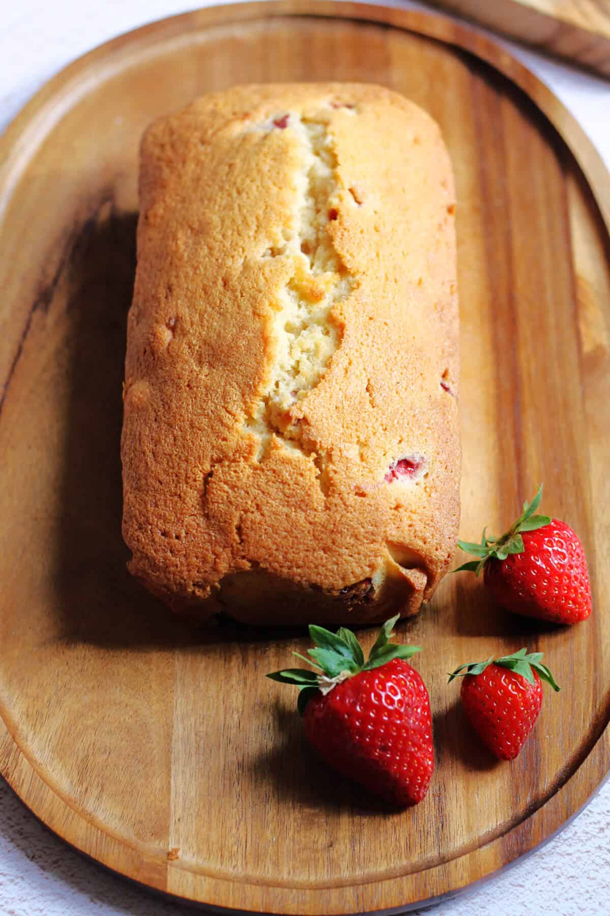 A loaf cake on a wooden platter, with some strawberries.